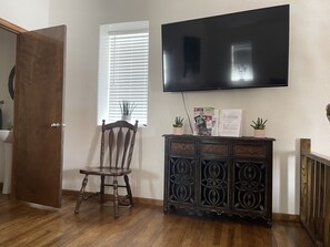 A room with a wooden floor, a wooden chair, a cabinet with decorative patterns, a flat-screen TV mounted on the wall, and a window with blinds. - 4 bedrooms 3 bath, Tranquil Home, Master suite & Jet tub, Mins from Hot Springs (Thermopolis)
