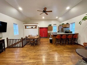 Une cuisine spacieuse avec des meubles de rangement en bois, un coin repas avec une table ronde et des chaises, un bar avec des tabourets et un ventilateur de plafond.