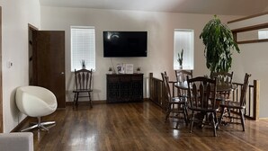 A spacious living room with a wooden floor, a dining table with chairs, a flat-screen TV mounted on the wall, and a large potted plant. - 4 bedrooms 3 bath, Tranquil Home, Master suite & Jet tub, Mins from Hot Springs (Thermopolis)