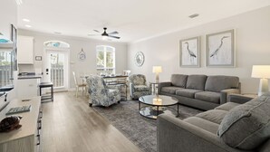 Uma sala de estar moderna com um sofá cinza, poltronas estampadas, uma mesa de centro e um espaço de jantar com mesa e cadeiras.