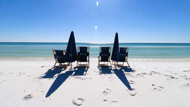 A beach with four lounge chairs and umbrellas, facing the ocean.