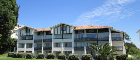 A multi-story residential building with balconies, surrounded by well-maintained lawns and hedges.