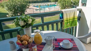 A breakfast setup on a balcony overlooking a pool and garden. - Bon Rapport Qualité-Prix! Appartement Duplex (Bidart)
