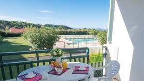Ein Balkon mit einem Frühstückstisch, Blick auf einen Swimmingpool und eine grüne Landschaft im Hintergrund.