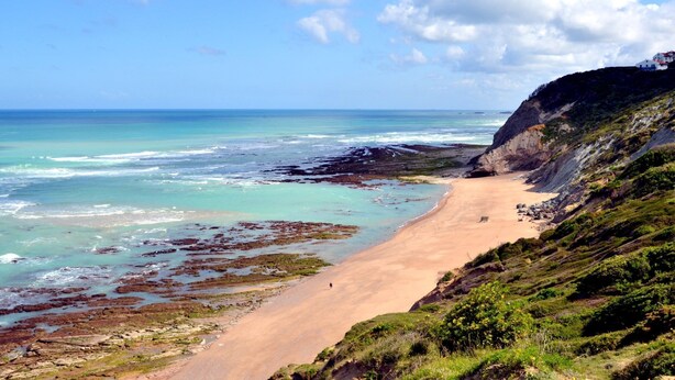 Eine Küstenlandschaft mit Sandstrand, Felsen und blauem Himmel.