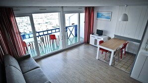 A modern room with a sofa, a dining table with chairs, a TV, and a balcony with a railing.
