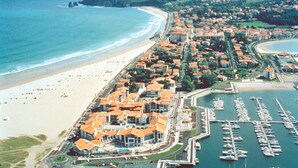 An aerial view of a coastal town with a marina, beach, and residential buildings with orange roofs.
