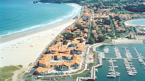 Luftaufnahme einer Küstenstadt mit Hafen, Strand und Wohnhäusern mit orangenen Dächern.