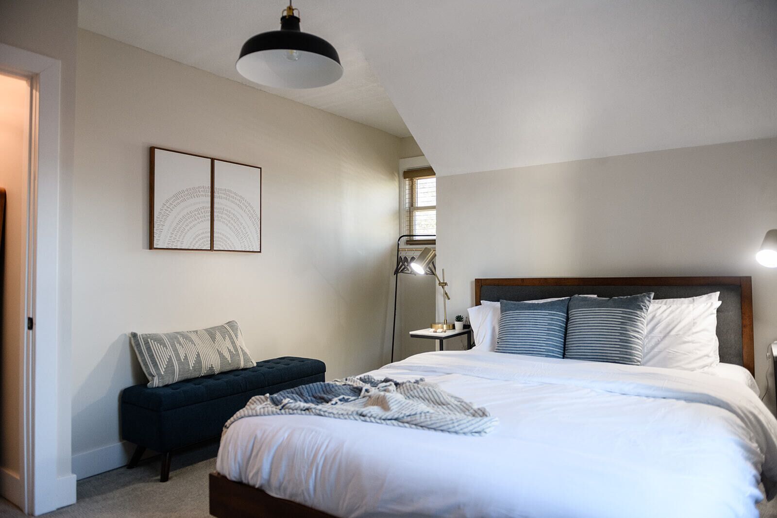 A bedroom with a large bed, a bedside table, a floor lamp, and a dark-colored bench.