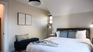 A bedroom with a large bed, a bedside table, a floor lamp, and a dark-colored bench.