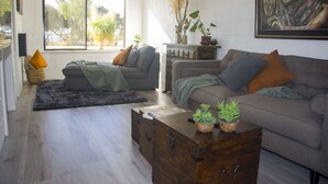 A living room with a sofa, a coffee table, and a wooden chest of drawers. There are plants on the coffee table and a painting on the wall.
