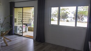 A room with a large sliding glass door leading to an outdoor area, a small table with a plant, and a window with a view of trees and a body of water.