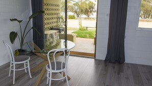 A modern room with a glass table and chairs, a potted plant, and a view of a garden and street outside.