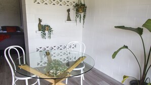 A dining area with a glass-top table, white chairs, and a potted plant.