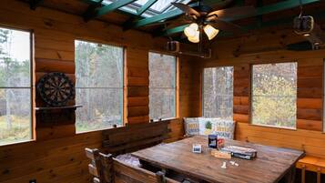 L’intérieur d’un chalet en bois comprend une table à manger, des chaises, un jeu de fléchettes et un ventilateur de plafond.
