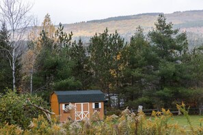 A small wooden cabin with a dark roof, surrounded by dense trees and a hilly landscape in the background. - Luxurious Mt Retreat Sauna Hot Tub Fire Pit & Park (Windham)