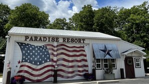 A building with a sign reading "Paradise Resort" and a large American flag painted on the side. - Enjoy the beautiful views of the Muskegon River near The Hardy Dam/ Dragon Trail (Newaygo)