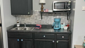 A compact kitchen with dark cabinets, a double sink, a microwave, a coffee maker, and a small refrigerator. - Enjoy the beautiful views of the Muskegon River near The Hardy Dam/ Dragon Trail (Newaygo)