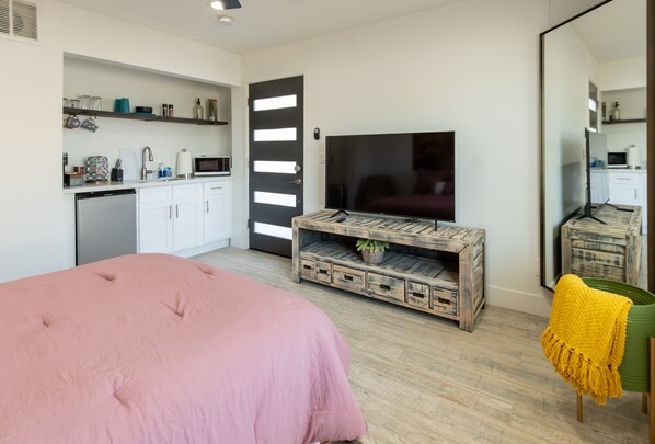 A modern bedroom with a pink bed, a wooden TV stand, and a large mirror.