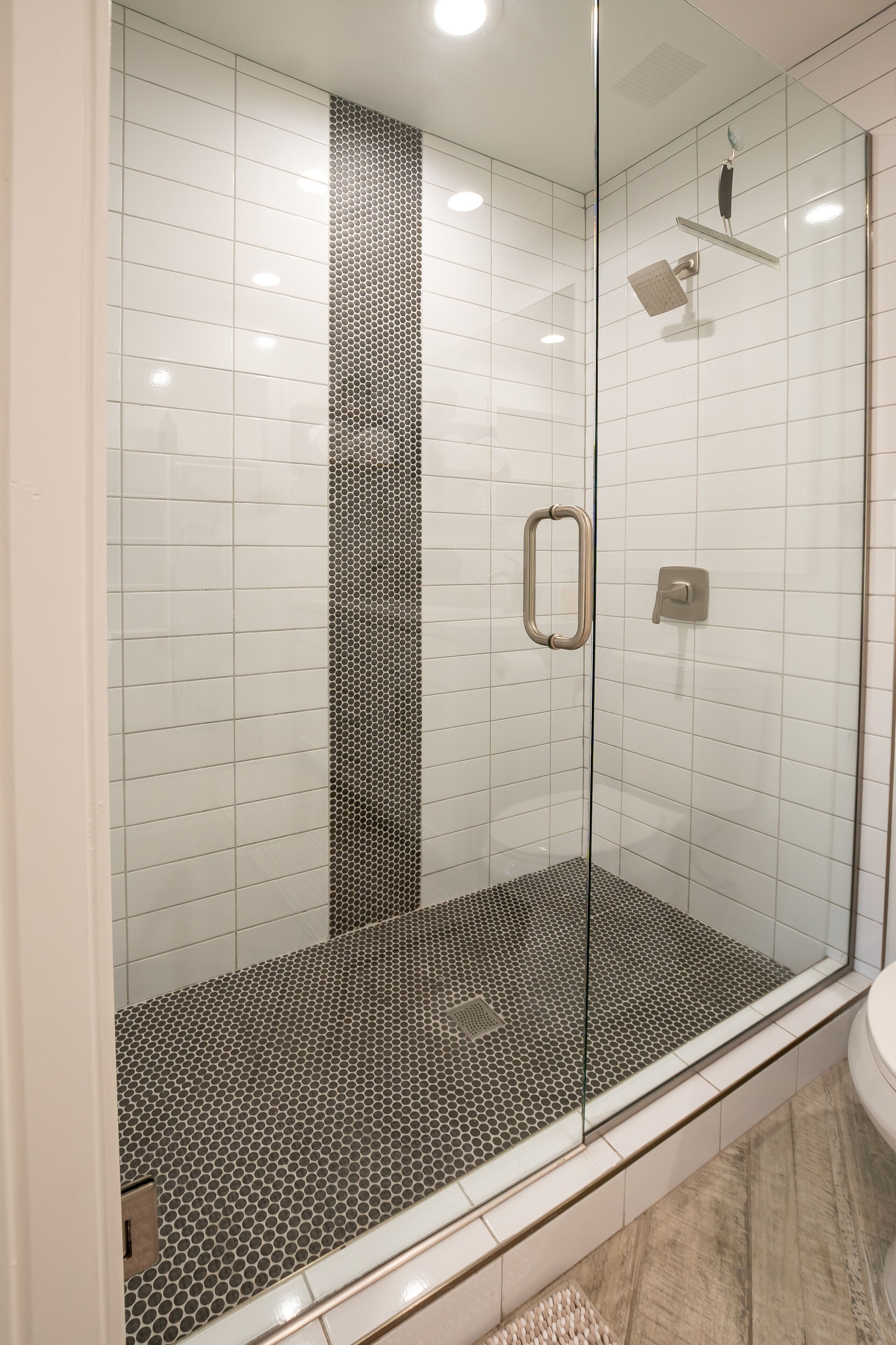 Eine gläserne Dusche mit gefliestem Boden und einer vertikalen Wand mit Schwarz-Weiß-Muster.