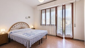 Ein Schlafzimmer mit einem Bett, Nachttischen, einem Fenster mit Vorhängen und einer Deckenleuchte.