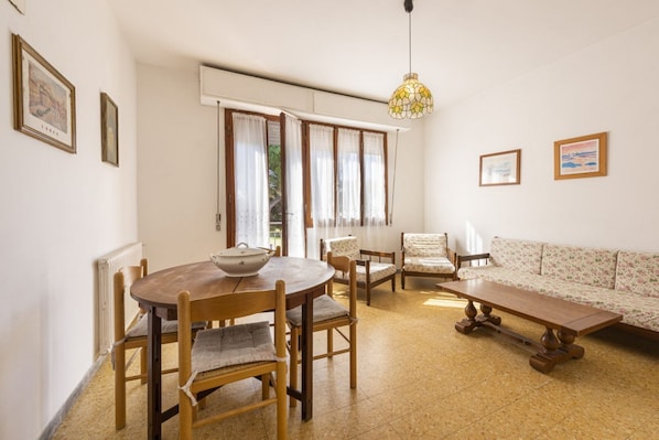 A dining area with a round table, chairs, a bench, a sofa, and a hanging light fixture.