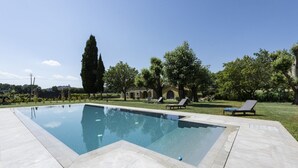 Piscina retangular com deck ladrilhado, rodeada por gramado e árvores.