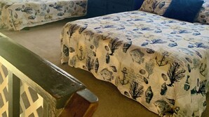 Une chambre à coucher avec deux lits, chacun recouvert d’une couvre-lit à motifs, une commode, un ventilateur et un tableau accroché au mur.