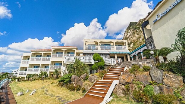 Um hotel com várias varandas, uma escadaria que leva à entrada e uma paisagem rochosa.