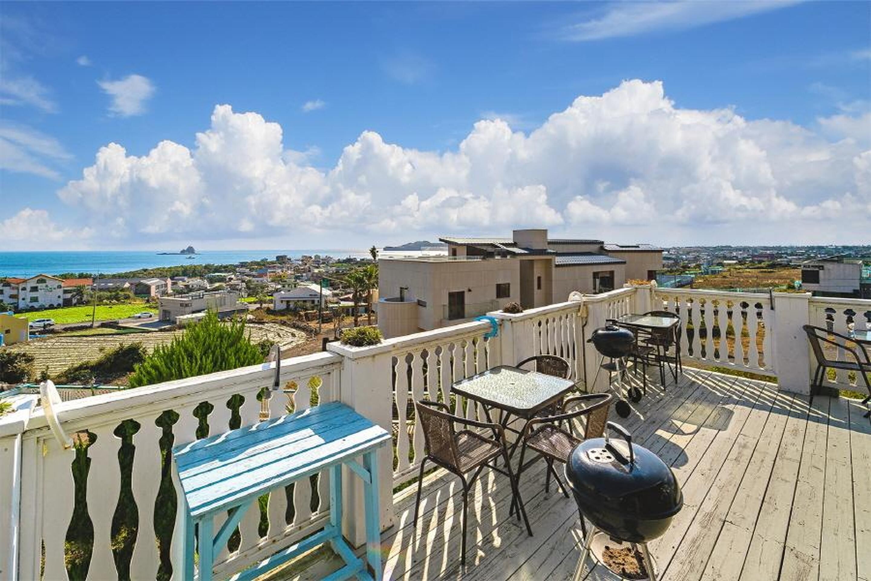 Une terrasse avec coin salon extérieur et barbecue, offrant une vue sur une ville côtière.