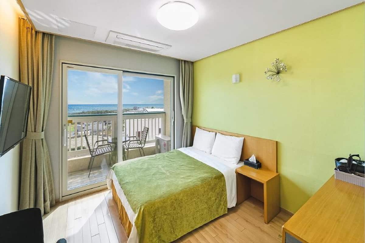 Une chambre d’hôtel avec un lit, une petite table, une télévision et un balcon donnant sur la plage.