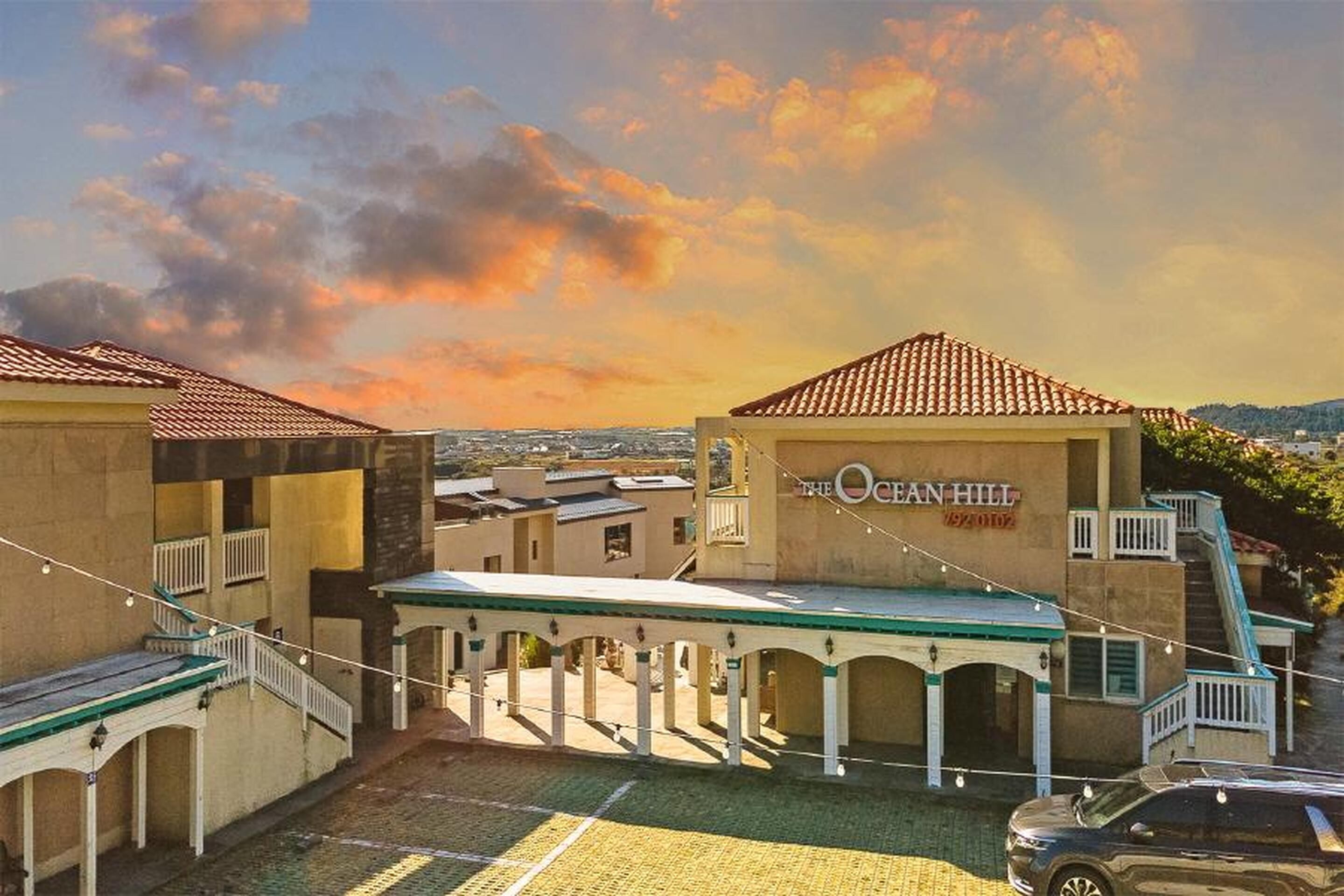 A hotel with a covered outdoor area, a sign reading "The Ocean Hill," and a view of the surrounding landscape.