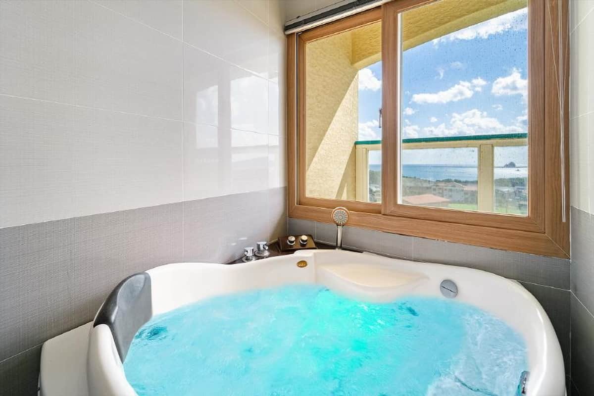 Une salle de bain moderne avec une grande baignoire, une fenêtre donnant sur la mer et un plafond en bois.