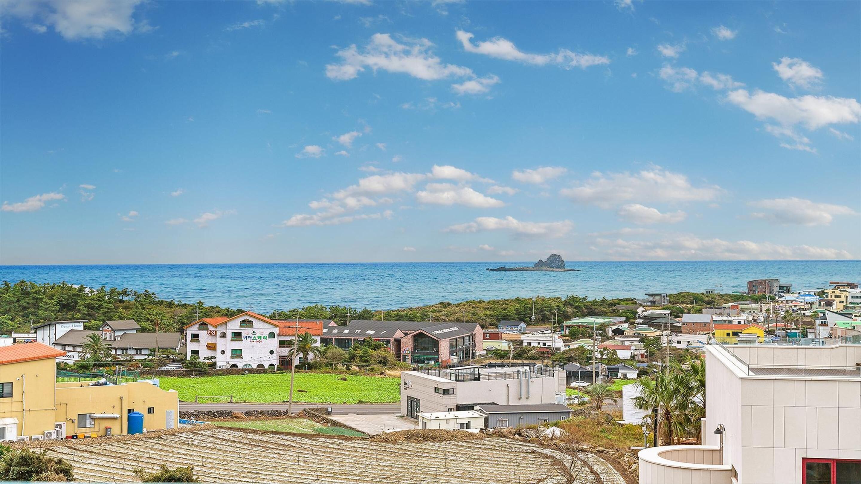 Eine Küstenstadt mit Gebäuden in Strandnähe, einem klaren Himmel und einer entfernten Insel.