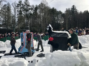Ett vinterevenemang utomhus med folk och en byggnad som är märkt med texten ”Stinkin’ Outhouse”.