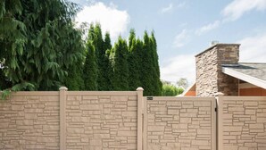 Un muro de piedra con una verja, una chimenea de piedra y altos árboles de hoja perenne.