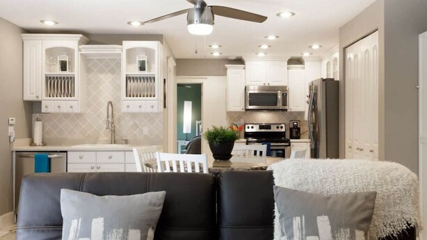 Una cocina moderna con gabinetes blancos, electrodomésticos de acero inoxidable y un ventilador de techo.