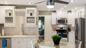 Una cocina moderna con armarios blancos, una isla central con asientos, un ventilador de techo y electrodomésticos integrados.