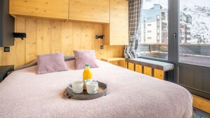 Un dormitorio acogedor con paredes de madera, una cama grande con ropa de cama rosa, una mesita de noche y una ventana con vistas a edificios.