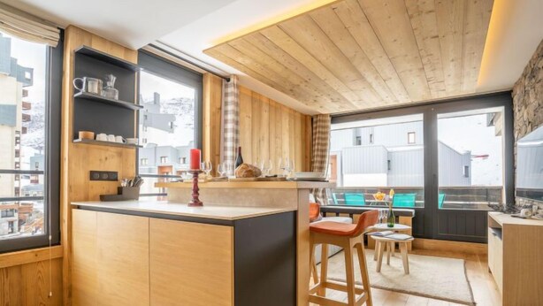Una cocina moderna con armarios de madera, una isla central y un comedor con taburetes de bar.