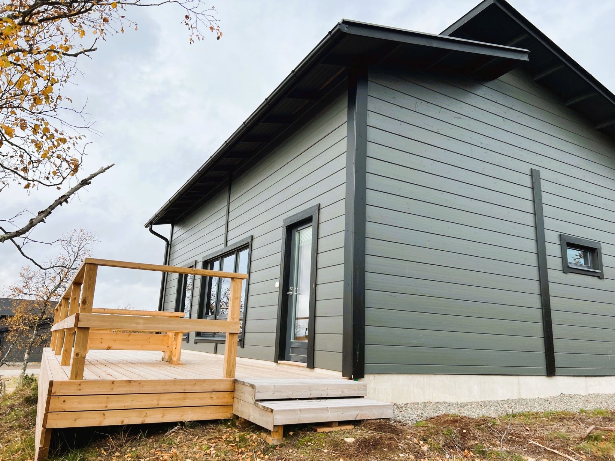 Een modern huis met twee verdiepingen, een houten terras en een betonnen fundering.