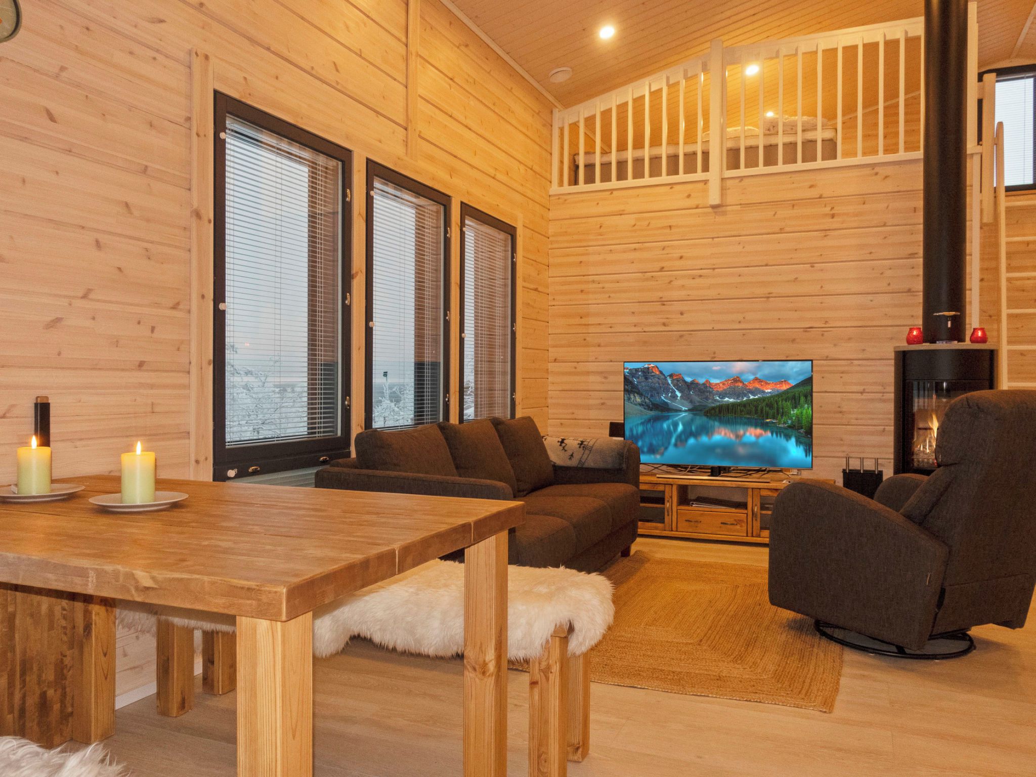 Un intérieur chaleureux en bois, avec un grand téléviseur à écran plat, une table à manger décorée de bougies et des sièges confortables.