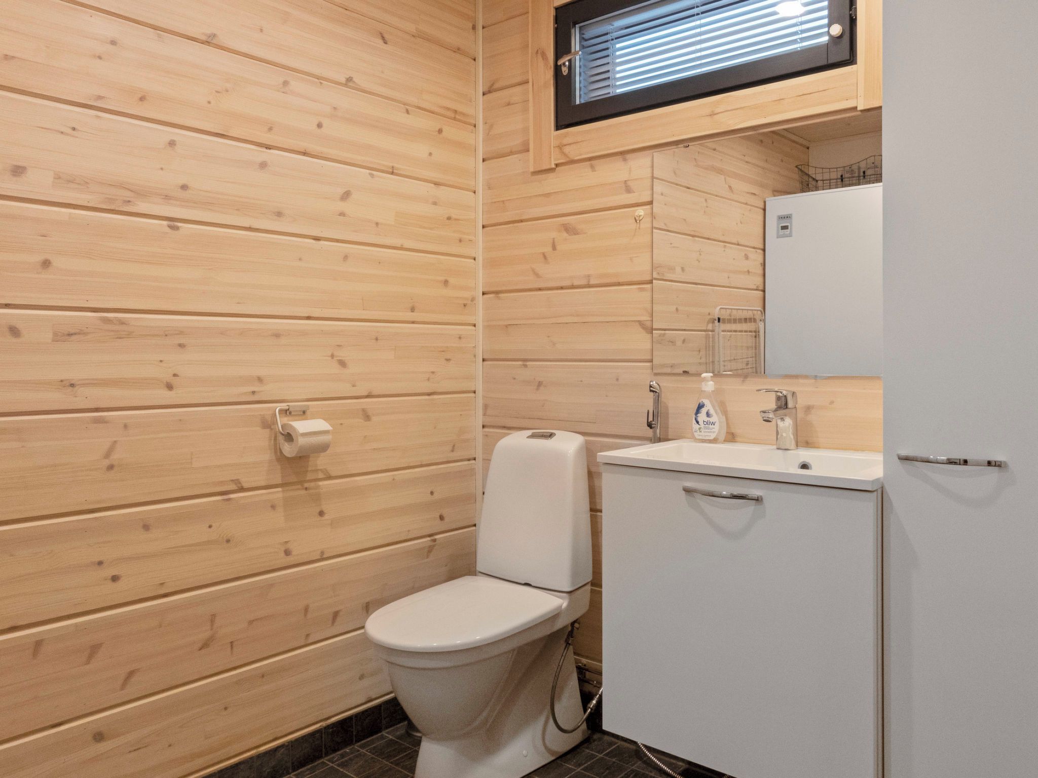 Ein Badezimmer mit Holzwandverkleidung, einer Toilette, einem Waschbecken und einem Fenster über dem Waschbecken.