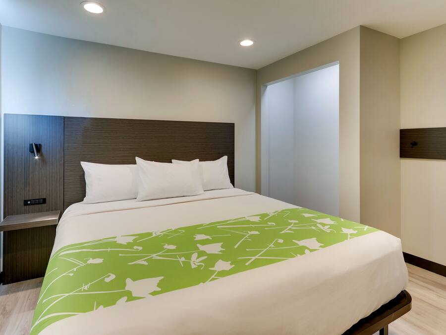 Een moderne hotelkamer met een groot bed, een nachtkastje en een bedtafel, plus een bedieningspaneel aan de muur.