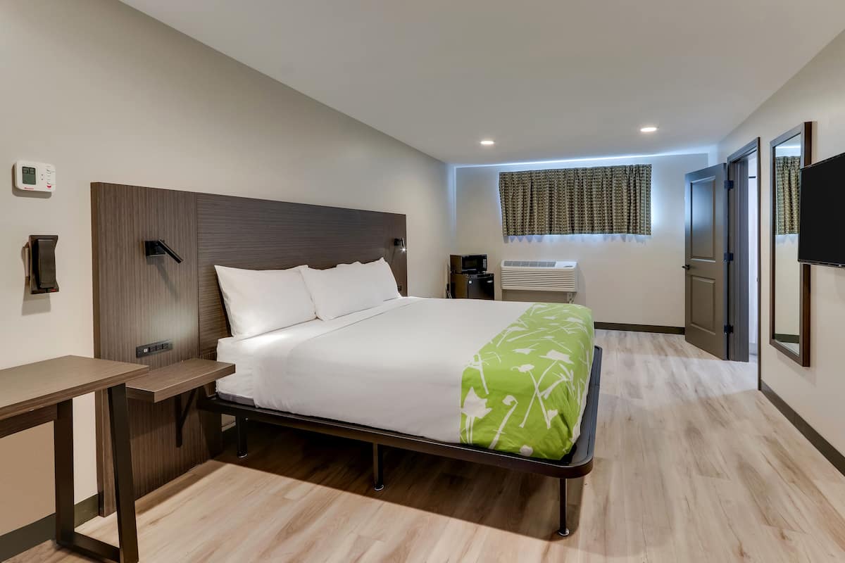 Una habitación de hotel moderna con cama, mesita de noche, televisor integrado, aire acondicionado y ventana con cortinas.