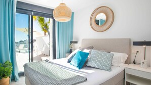 Un dormitorio con cama, mesita de noche, lámpara, espejo y vistas al exterior.