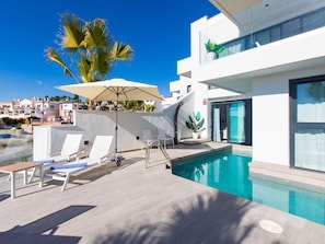 Uma área moderna com piscina ao ar livre, espreguiçadeiras, guarda-sol e vista desobstruída do bairro.