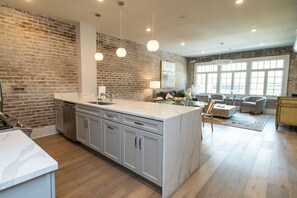 Una cocina con una isla grande, una pared de ladrillo y un comedor con sillas y una mesa.