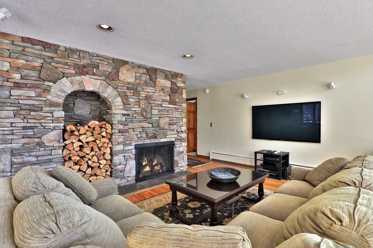 A living room with a stone fireplace, a large flat-screen TV, and a comfortable seating area.