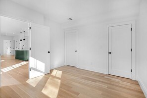 A spacious, well-lit hallway with wooden flooring and white walls, leading to multiple doors and a visible kitchen area. - Union Square Beauty 2 bed/2 bath w/ Private Patio (Somerville)